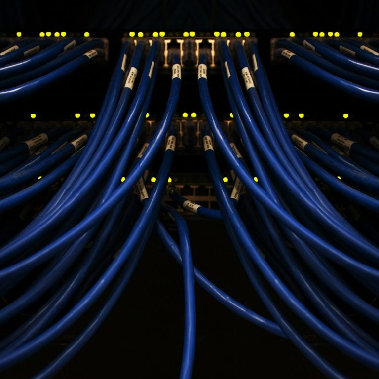 Kommunikationsanlagen Blaue Netzwerkleitungen mit gelben Leuchten, in einem dunklen Serverraum angeordnet.