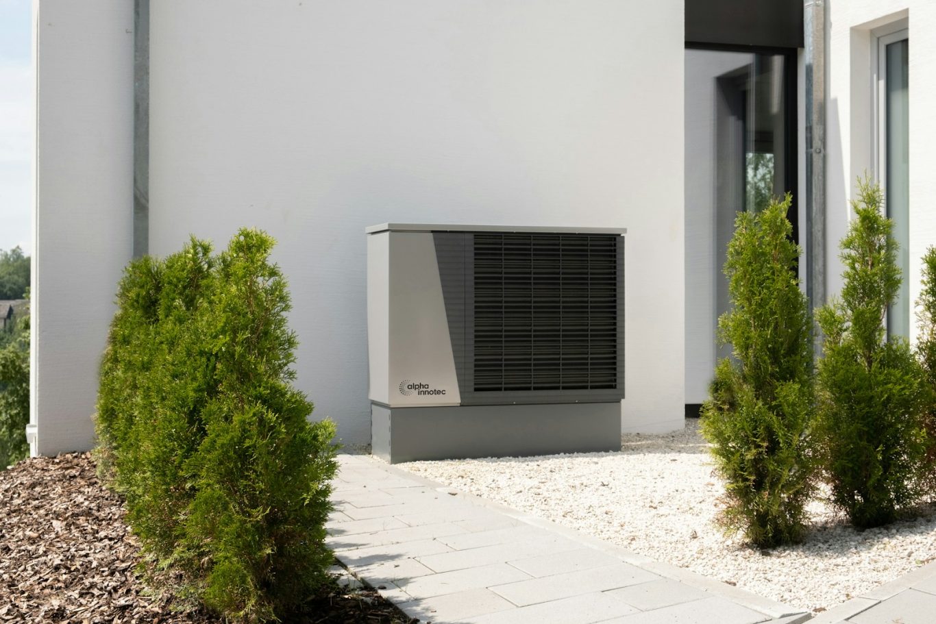 Wärmepumpe Außenanlage einer Klimaanlage neben einer modernen weißen Wand mit Sträuchern.