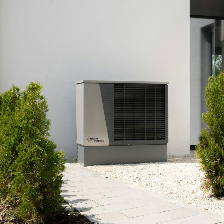 Wärmepumpe Wärmepumpe steht neben einem modernen Gebäude, umgeben von Gründerbüschen.