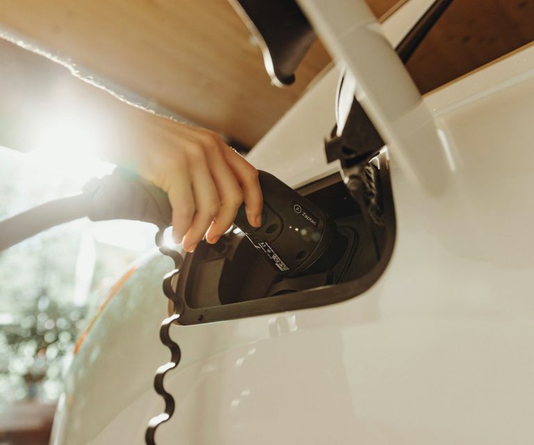 Hand steckt Stecker in Ladeanschluss eines Elektroautos.