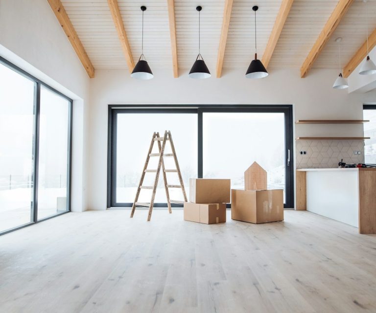 Heller Innenraum mit Holzleitern, Kisten und großen Fenstern.