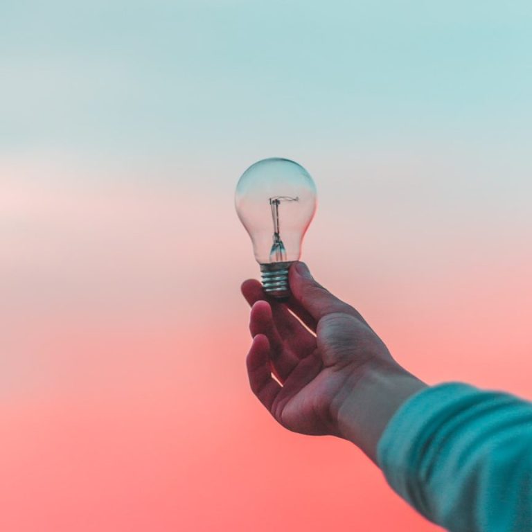 Licht-Design Eine Hand hält eine Glühbirne vor einem pastel hintergrund aus Himmel.